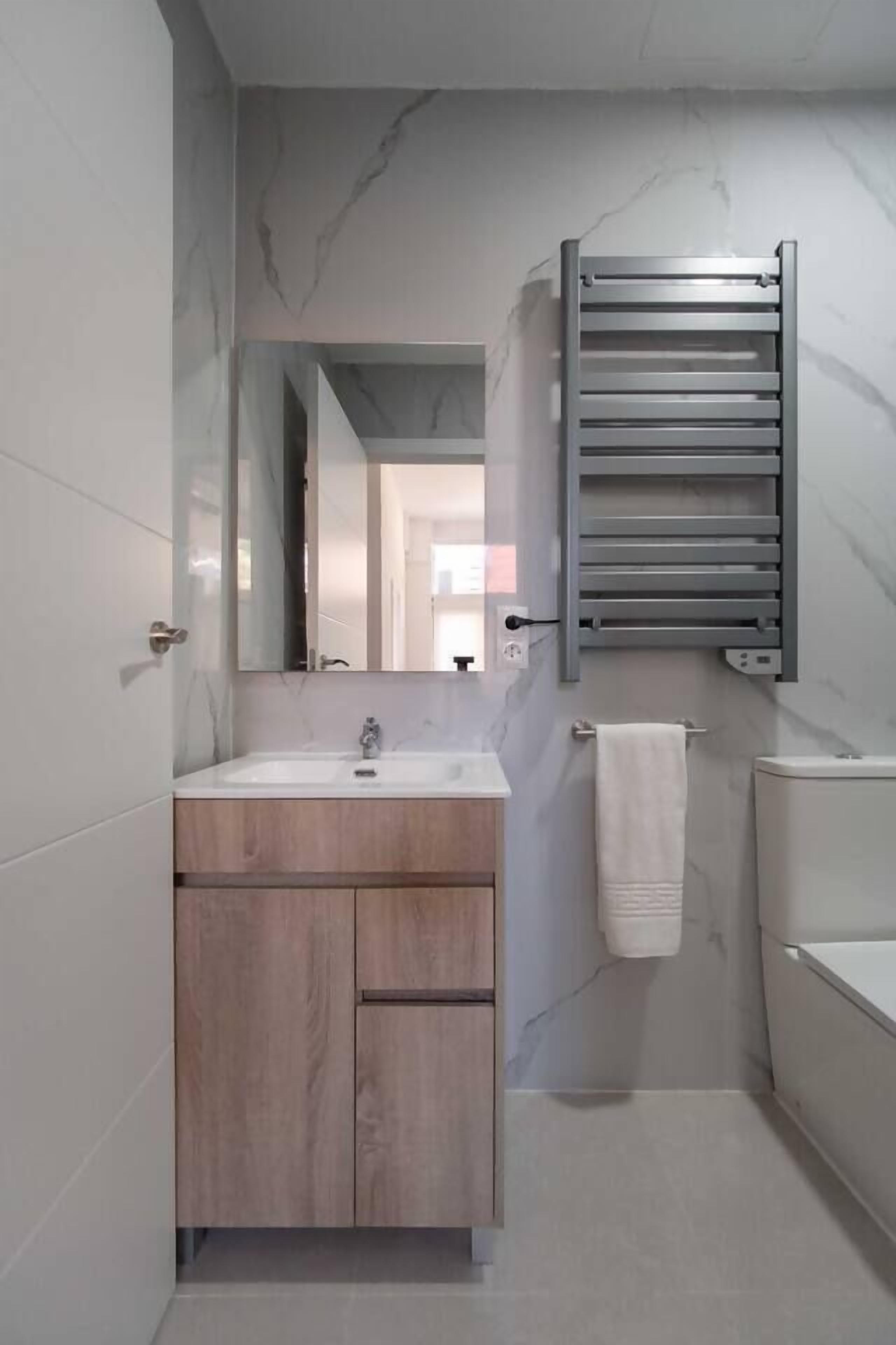 Een moderne badkamer met een marmeren wand, een houten wastafelmeubel, een handdoekhouder en een toilet.