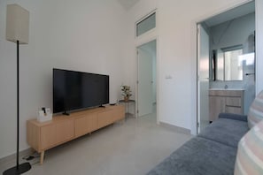 A modern living room with a flat-screen TV on a wooden cabinet, a small side table with a plant, and a grey sofa. - Portazgo Apartment | 2 Bedrooms + Sofa Bed (Madrid)