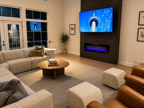 Ein modernes Wohnzimmer mit einem Ecksofa, einem runden Couchtisch, einem Flachbildfernseher an einer dunklen Wand und einem Kamin.