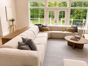A modern living room with a sectional sofa, a coffee table, and a view of a garden through large windows. - Luxurious Hidden Gem in Suburbs of Cleveland OH (Gates Mills)
