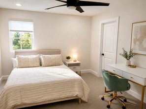 Ein Schlafzimmer mit Bett, Nachttisch, Lampe, Schreibtisch, Stuhl und Deckenventilator.