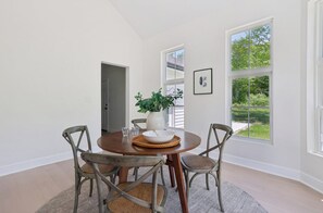 A dining area with a round table, four chairs, a vase, and a bowl. There are two windows with views of greenery. - Luxurious Hidden Gem in Suburbs of Cleveland OH (Gates Mills)