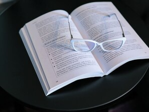 En öppen bok med ett par glasögon ovanpå, placerad på en svart yta.