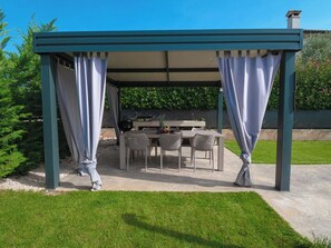 A covered outdoor seating area with a table and chairs, surrounded by greenery and a clear sky. - Villa Maslina by Interhome (Dracevac)