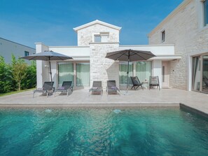 A modern outdoor pool area with lounge chairs and umbrellas, surrounded by a stone building with large windows. - Villa Lavanda by Interhome (Poreč/Nova Vas)