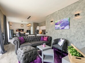 A modern living room with a grey sectional sofa, a small table, and a chair. There is a kitchen in the background with a fridge, oven, and cabinets. - Villa Lavanda by Interhome (Poreč/Nova Vas)