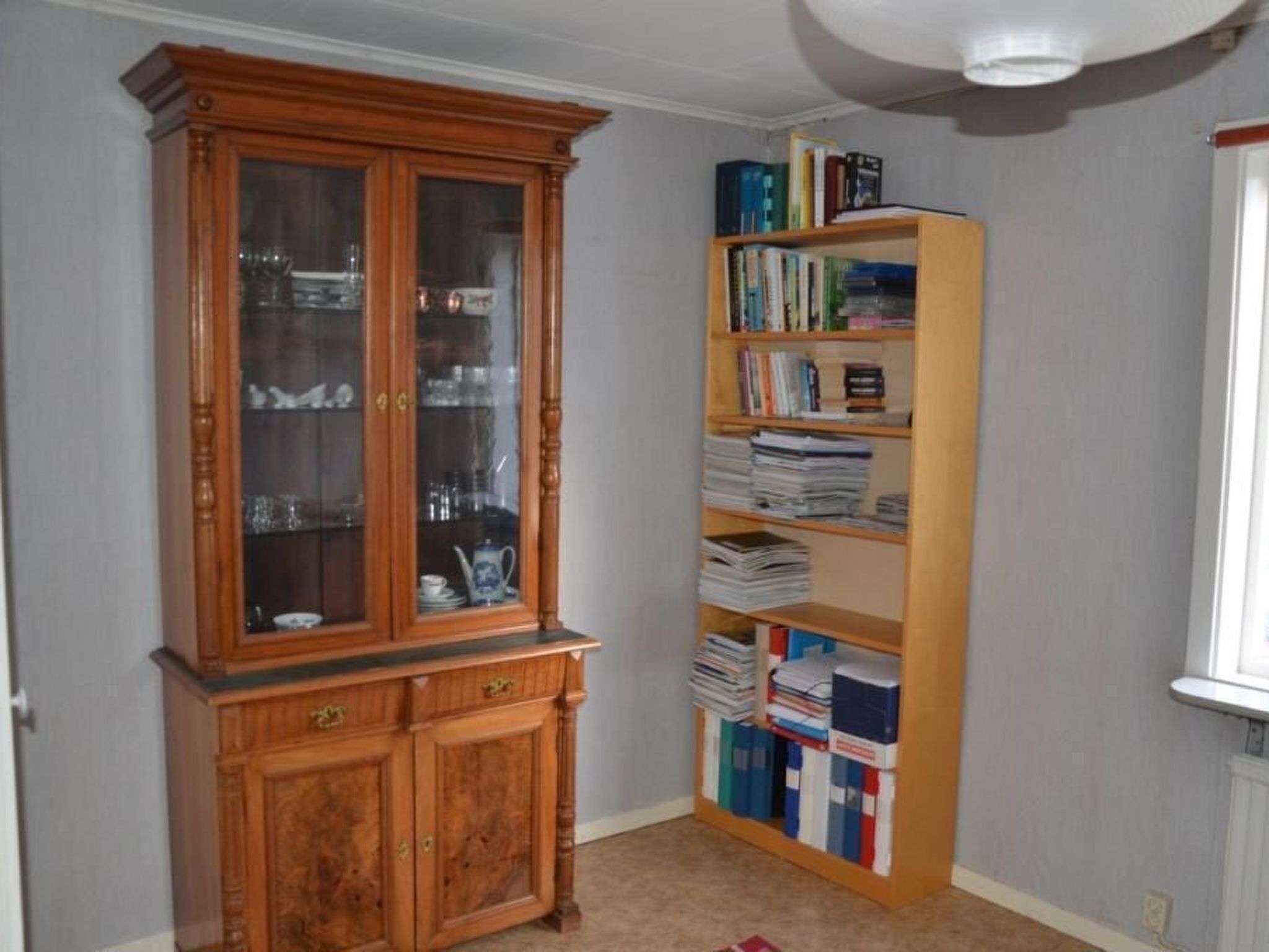 A room with a wooden cabinet and a tall bookshelf filled with books and binders.