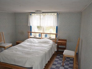 Ein kleines Zimmer mit einem Einzelbett, einem Holzbettgestell, einem Nachttisch, einem Stuhl und einem fenster mit Vorhängen.