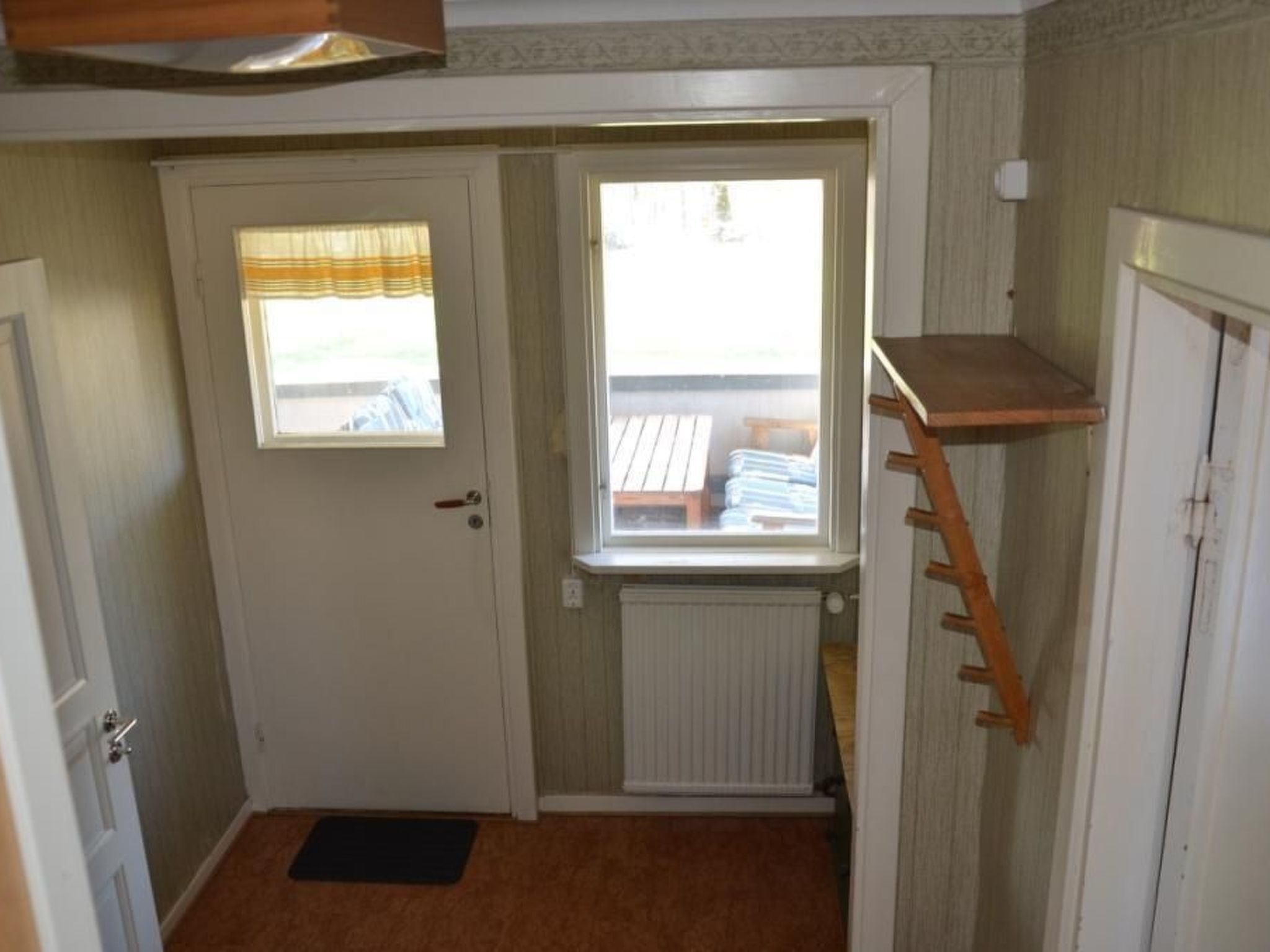 Habitación pequeña con una puerta, una ventana, un radiador y un estante de madera.