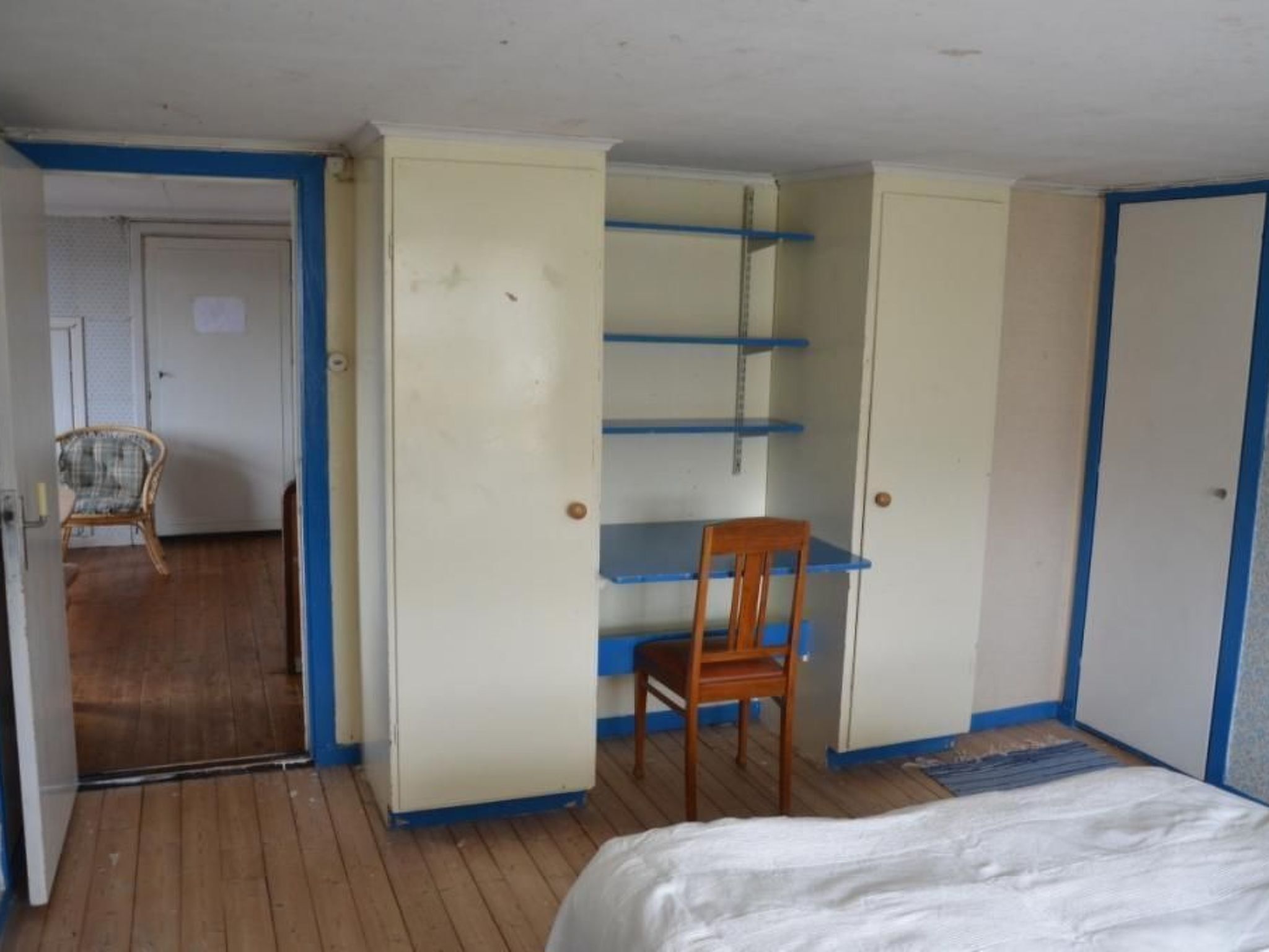 A bedroom with a bed, a wooden chair, and a wardrobe with shelves.