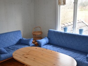Ein Zimmer mit einem blauen Sofa, einem Holztisch und einem Korbstuhl.