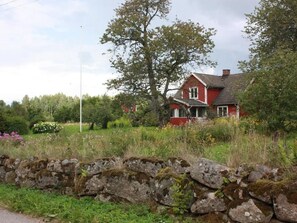 A red house with a stone wall in the foreground. - Schönes Ferienhaus in Småland mit Sauna, Bootssteg zum Schwimmen mit Ruderboot by Interhome (Tingsryd)