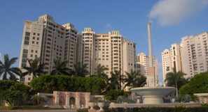A high-rise residential building with a central monument, surrounded by greenery and palm trees. - Cape Marco Paradise: Beachfront Monterrey Condo, #302 with 2 Balconies (Marco Island)