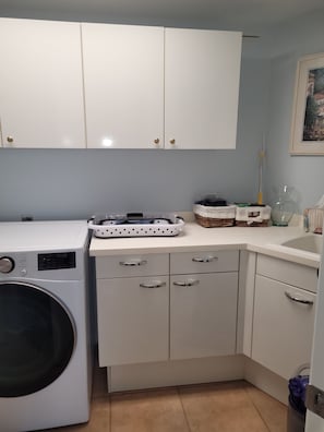 A laundry area with a washing machine, cabinets, and a countertop with baskets and a vase. - Cape Marco Paradise: Beachfront Monterrey Condo, #302 with 2 Balconies (Marco Island)