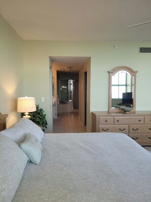 A hotel room with a bed, a dresser, a mirror, and a hallway leading to a bathroom. - Cape Marco Paradise: Beachfront Monterrey Condo, #302 with 2 Balconies (Marco Island)