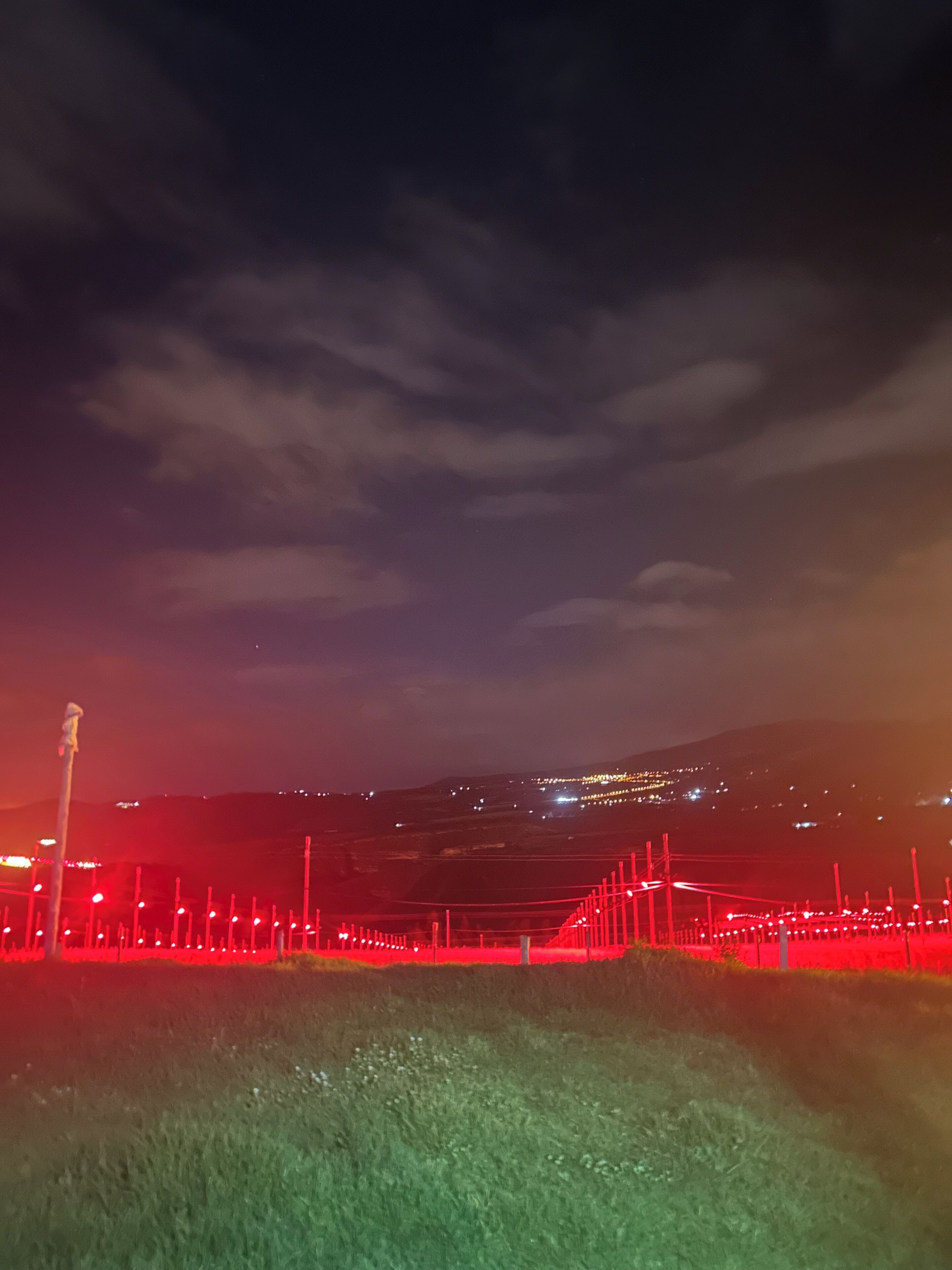Un paysage nocturne avec une colline lointaine et une clôture illuminée de lumière rouge.