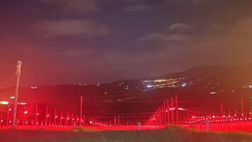 Un paysage nocturne avec une colline lointaine et une clôture illuminée de lumière rouge.