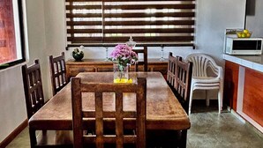 A dining area with a wooden table and chairs, a vase with flowers, a clock on the wall, and a microwave on the counter. - Unique Flower Farm Stay near Cayambe Fireplace & BBQ (Pichincha)