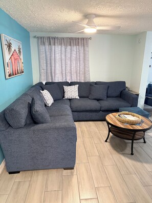 A living room with a sectional sofa, a round coffee table, and a ceiling fan. - Coral cottage 2 miles form the beach bring your boat (Englewood)