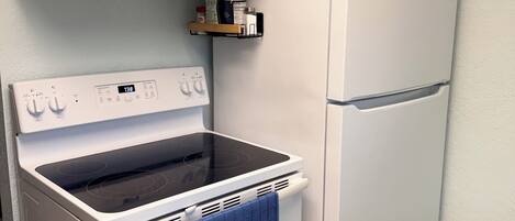A kitchen with a white stove, a white refrigerator, teal cabinets, and a small shelf with kitchen items.