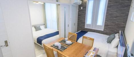 A compact hotel room with a bed, a small dining table with chairs, a TV, and a window with curtains.