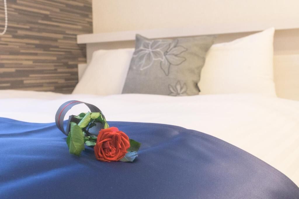 A bed with a blue bedspread, a decorative pillow with a floral design, and a rose on the bed.