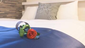 A bed with a blue bedspread, a decorative pillow with a floral design, and a rose on the bed.