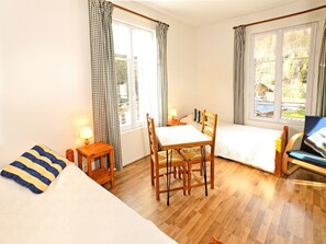 A room with a bed, a table with chairs, a lamp, and a view of the outdoors through the windows.