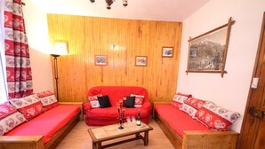 A cozy living room with a red sofa set, wooden flooring, and a wooden wall panel.