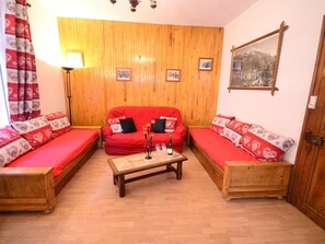 A cozy living room with a red sofa set, wooden flooring, and a wooden wall panel.