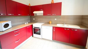 A compact kitchen with red cabinets, a white microwave, a stove, and a sink.