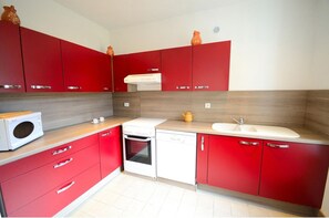 A compact kitchen with red cabinets, a white microwave, a stove, and a sink.