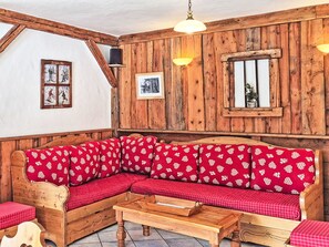 A wooden interior with a red patterned sofa, wooden walls, and a small table. - Chalet de la Cote by Interhome (Champagny-en-Vanoise)