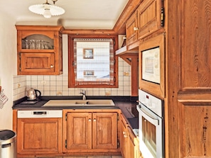 A kitchen with wooden cabinets, a Bosch dishwasher, a stove, and a window with a patterned curtain. - Chalet de la Cote by Interhome (Champagny-en-Vanoise)