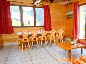 A wooden interior with a dining table and six chairs, a bottle of wine, and a painting on the wall. - Chalet Carella by Interhome (Champagny-en-Vanoise)