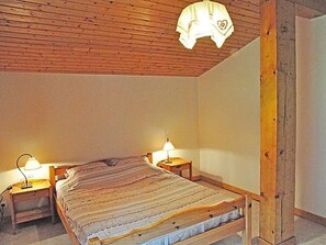Ein Schlafzimmer mit Holzboden, einem Bett mit Streifenmusterdecke, zwei Nachttischlampen und einem Nachttisch.