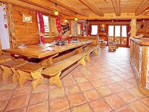 A wooden interior with a long dining table set for a meal, benches, and a fireplace. - Chalet Le Haut by Interhome (Champagny-en-Vanoise)