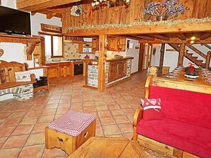 A rustic interior with a wooden dining table, a red sofa, and a kitchen area. - Chalet Le Haut by Interhome (Champagny-en-Vanoise)