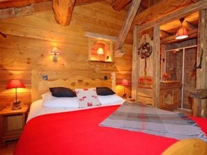 Ein Schlafzimmer einer Holzhütte mit einem Bett, zwei Nachttischlampen, einem Nachttisch und einem Fenster mit Vorhängen.
