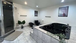 Ein modernes Badezimmer mit einer großen, schwarzen Jacuzzi-Badewanne, einer Duschkabine aus Glas und einem Topf mit einer Pflanze.