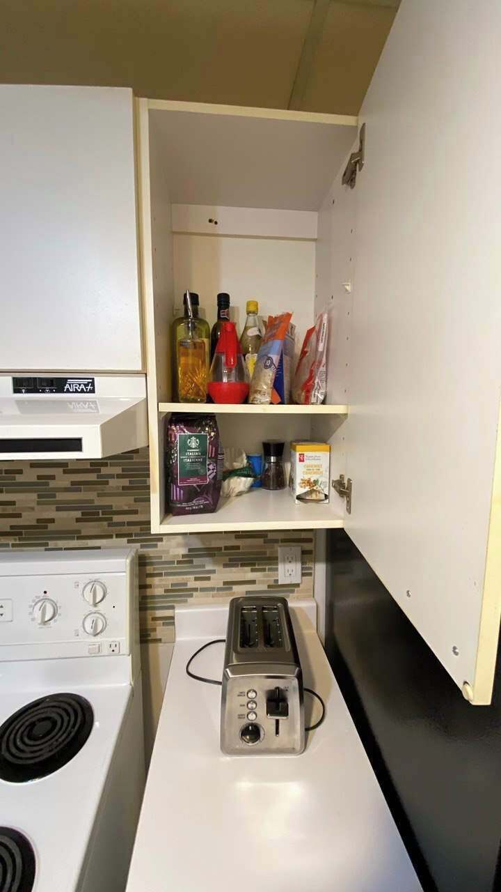 Une petite cuisine équipée d’une cuisinière, d’un grille-pain et d’un petit placard contenant divers aliments et condiments.