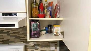 Une petite cuisine équipée d’une cuisinière, d’un grille-pain et d’un petit placard contenant divers aliments et condiments.