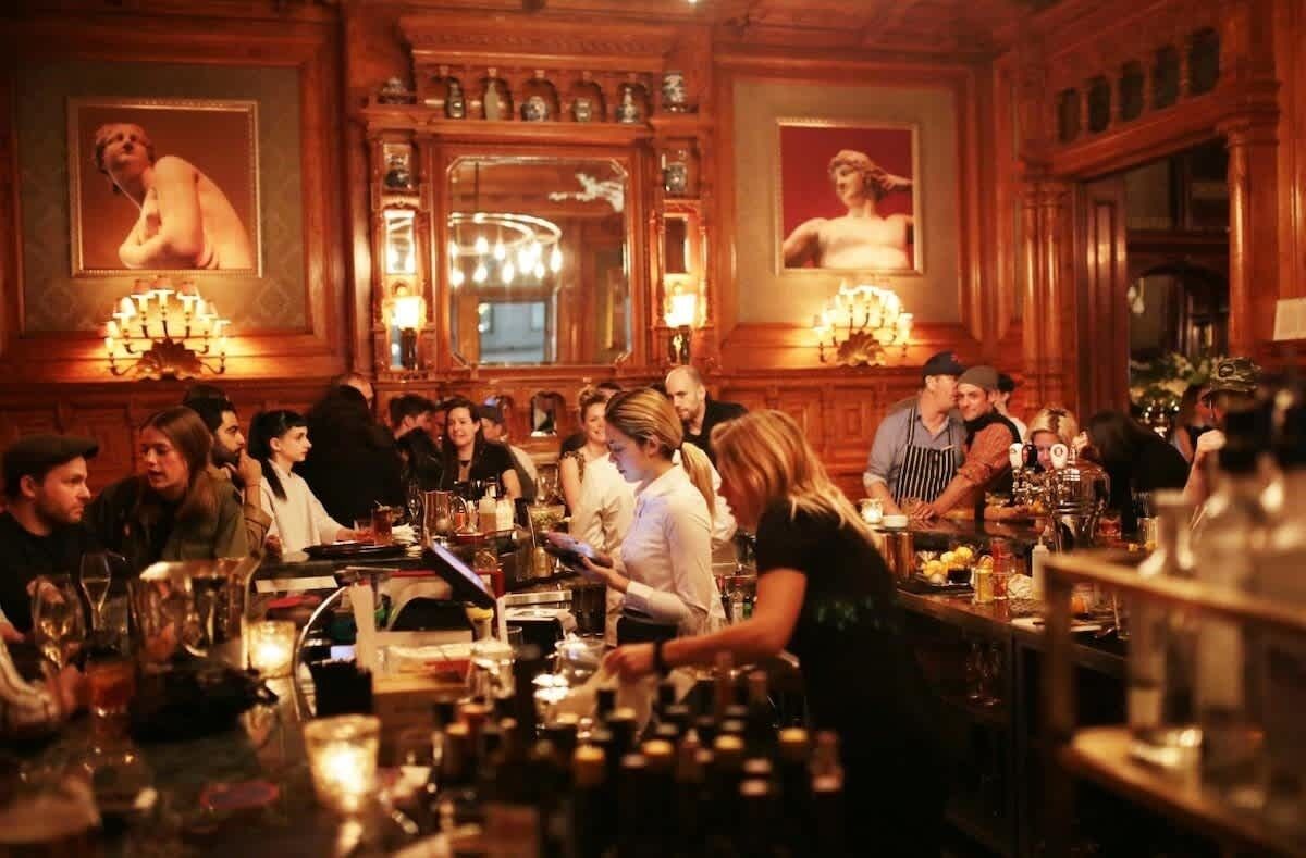 A bar area with patrons and staff, wooden decor, and framed artwork on the walls.