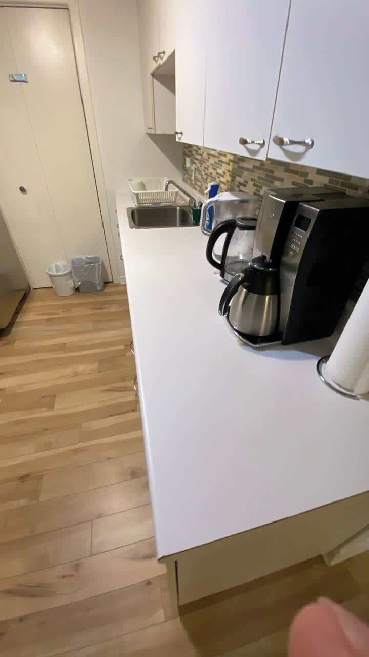 A kitchen with a white countertop, a coffee maker, and a sink.