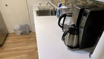 A kitchen with a white countertop, a coffee maker, and a sink.