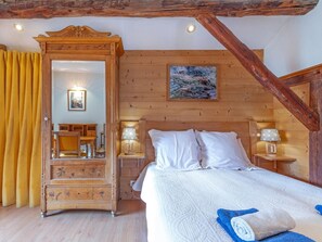 Ein Schlafzimmer mit einem hölzernen Himmelbett, einem großen Spiegel, einem Bild an der Wand und einem gelben Vorhang.