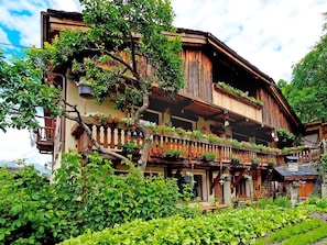 Ein traditionelles Holzchalet mit mehreren Balkonen, umgeben von üppigem Grün und einem gepflegten Garten.