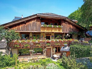 Eine Holzhütte mit einem Balkon, der mit Blumen geschmückt ist, eine Steinsäule und ein Garten.