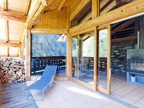 Uma cabana de madeira com varanda, uma cadeira de descanso e lareira de pedra.