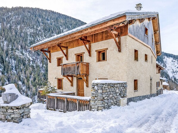 Ein Chalet-Stil Gebäude mit steinernem Fundament, Holzbalkonen und einer verschneiten Landschaft.